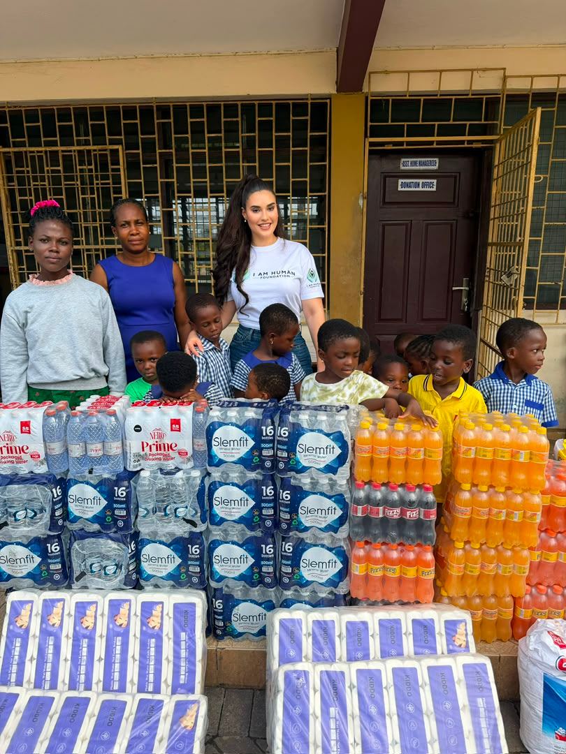 Shalimar Abbiusi and volunteers standing behind stacked cases of bottled water and supplies with schoolchildren