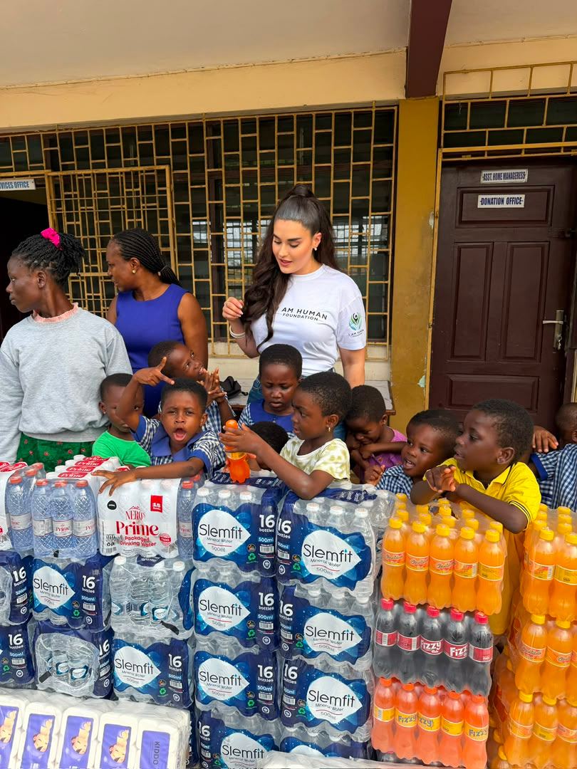 Volunteers and children beside a delivery of water, drinks and sanitary supplies at a school