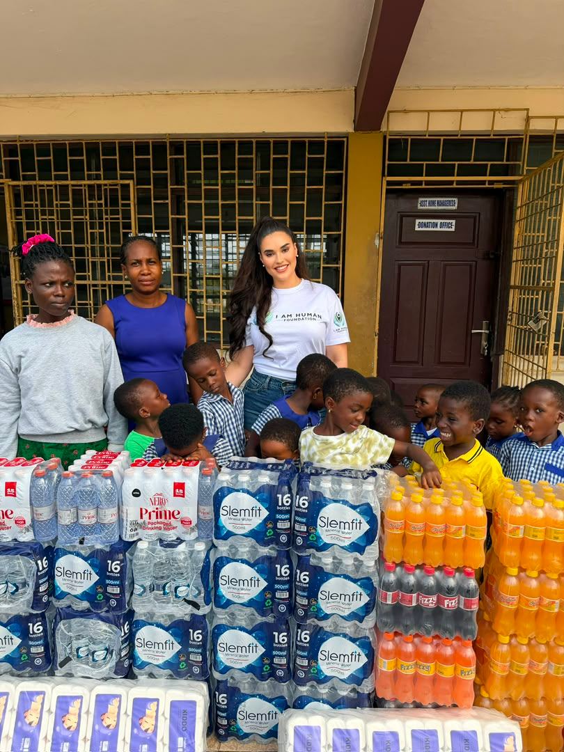 Donated supplies stacked outside a school building with pupils and volunteers behind them