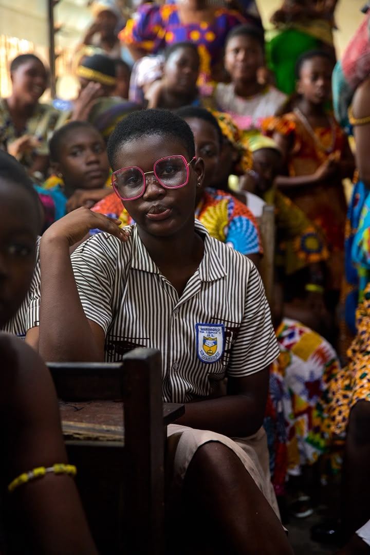 A schoolgirl seated among classmates during a community meeting