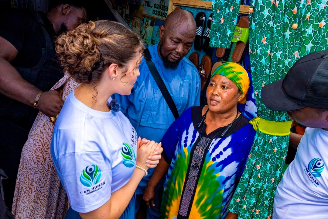 Shalimar Abbiusi in an I Am Human Foundation shirt greeting a trader at a fabric stall