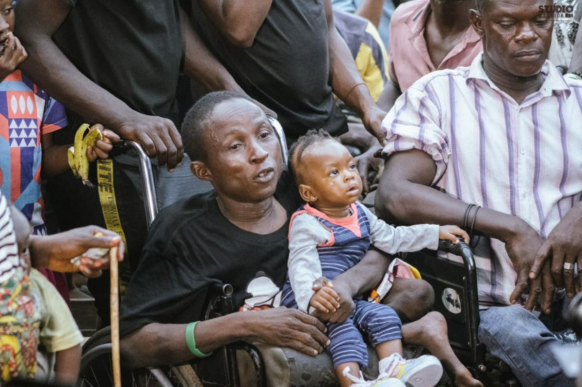 A man using a wheelchair holding a small child at a street distribution